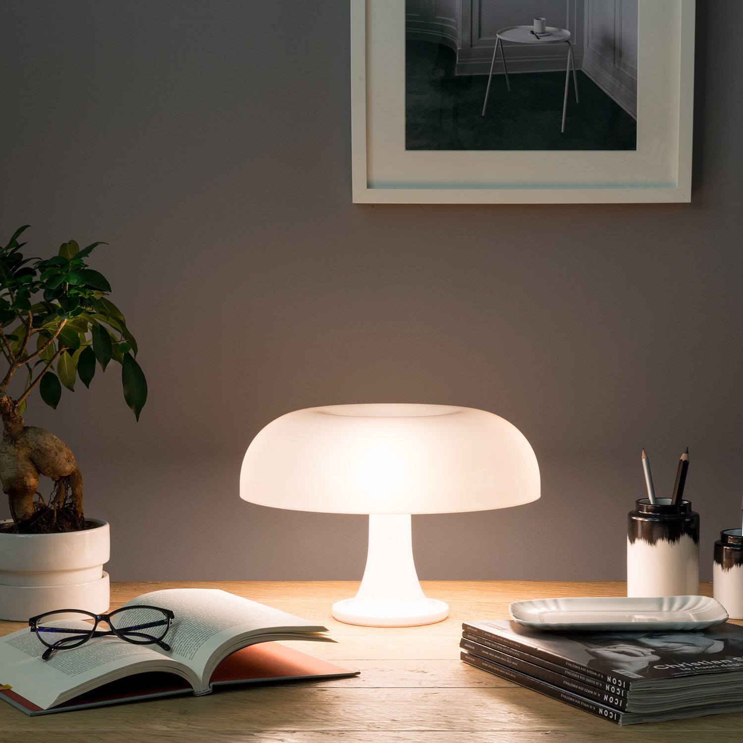 Artemide Nessino Table Lamp ambient image showing white version lit up on a desk